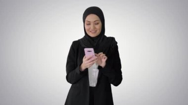 Gülümseyen Arap kadın gradyan arka planda akıllı telefon kullanıyor.