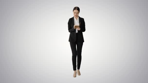Femme concentrée dans un costume écrivant des idées d'affaires dans son bloc-notes tout en marchant sur fond de dégradé. — Video
