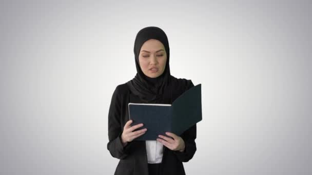 Empresaria musulmana leyendo a su planificador de negocios mientras camina a la reunión sobre el fondo de gradiente. — Vídeos de Stock