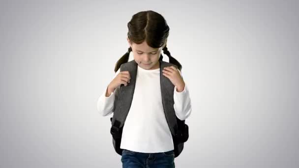 Lächelndes kleines Mädchen, das mit dem Rucksack zur Schule läuft und in die Kamera auf dem Hintergrund des Gefälles schaut. — Stockvideo