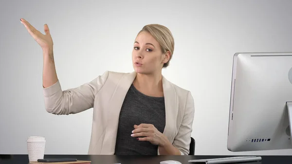 Senhora olhando e falando com a câmera em sua mesa de trabalho e apontando — Fotografia de Stock