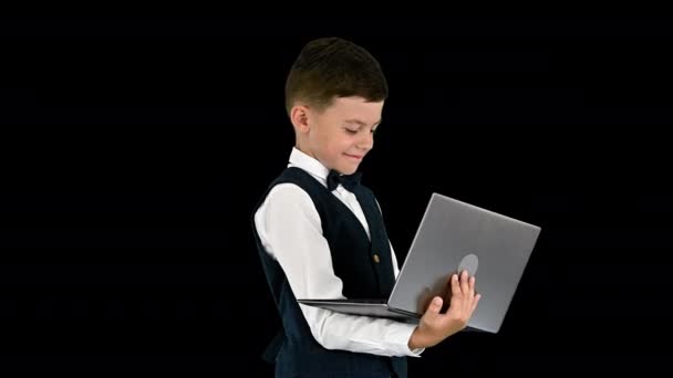 Smiling boy in a bow tie and waistcoat using laptop computer while standing, Alpha Channel — Stock Video