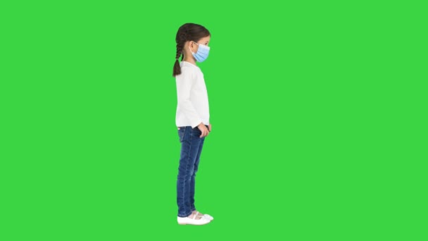 Liten flicka som tar av sig ansiktsmask och ler mot kameran på en grön skärm, Chroma Key. — Stockvideo