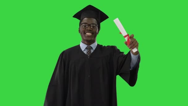 Šťastný africký americký student mužského pohlaví v maturitním županu kráčející s diplomem a mluvící s kamerou na zelené obrazovce, Chroma Key. — Stock video
