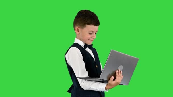 緑の画面、クロマキーに立っている間、弓ネクタイとノートパソコンを使用して腰のコートで笑顔の男の子. — ストック動画