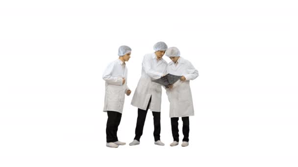 Trois médecins masculins en robes blanches et casquettes de protection regardant l'image de tomodensitométrie et pensant à la caméra sur fond blanc. — Video