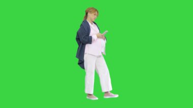 Güzel hamile bir kadın, akıllı telefonunu kullanarak karnına dokunuyor. Yeşil ekranda, Chroma Key 'de duruyor..