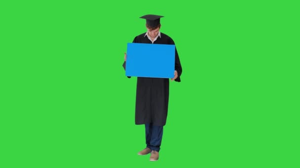 Lächelnder Absolvent in Mörtelpappe mit leerem Schild und Blick auf einem Green Screen, Chroma Key. — Stockvideo