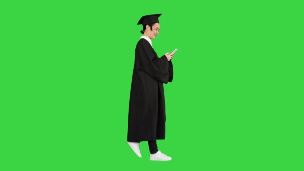 Leende kvinna examen i kartong dela glada nyheter på sin telefon när du går på en grön skärm, Chroma Key. — Stockvideo