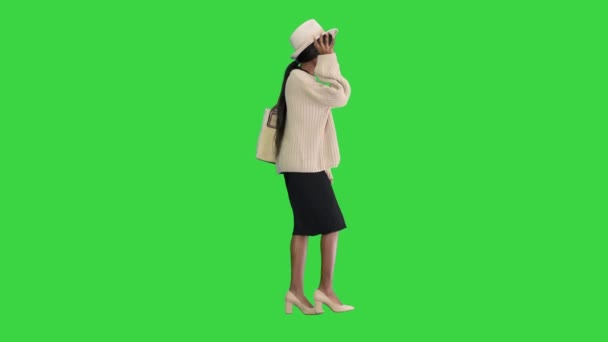 Örgü ve beyaz şapkalı gülümseyen Afrikalı Amerikalı kadın yeşil ekranda yürürken poz veriyor, Chroma Key. — Stok video