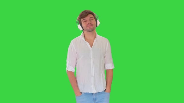 Zwykły młodzieniec w słuchawkach słuchający muzyki i cieszący się nią zamykający oczy na zielony ekran, Chroma Key. — Wideo stockowe