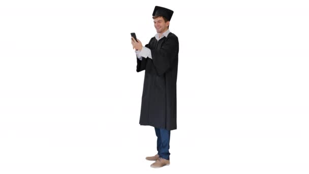 笑顔男性学生で卒業生ガウンショーキャンパスを経由してビデオ通話上の彼の電話上の白い背景. — ストック動画