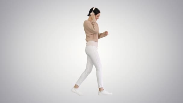 Mujer sonriente con auriculares caminando y bailando a la música sobre fondo degradado. — Vídeos de Stock