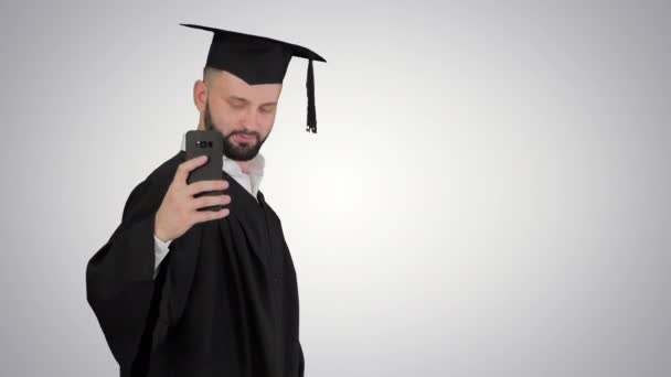 Muž na sobě maturitní župan chůzi a přičemž selfie s diplomem na gradient pozadí.