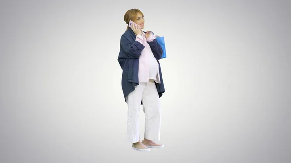 Счастливая беременная женщина делает покупки и разговаривает по телефону, держа в руках сумки — стоковое фото