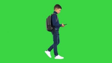Sırt çantalı öğrenci yeşil ekranda yürürken cep telefonu kullanıyor, Chroma Key.