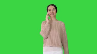 Gülümseyen genç kadın yeşil ekranda yürürken telefonda konuşuyor, Chroma Key.