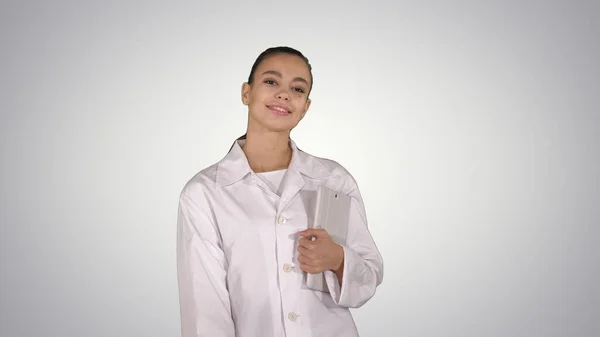 Mulher médico andando com comprimido nas mãos sobre fundo gradiente — Fotografia de Stock