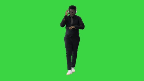 Jovem afro-americano ouvindo música em fones de ouvido e grooving enquanto caminha em uma tela verde, Chroma Key. — Vídeo de Stock