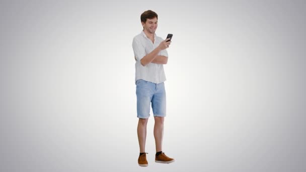 Joven guapo usando su teléfono inteligente y riéndose en un fondo degradado. — Vídeos de Stock