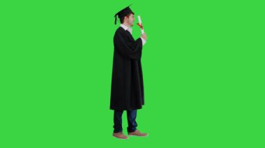 Mezuniyet cüppeli gülümseyen erkek öğrenci yeşil ekranda diplomasıyla poz veriyor, Chroma Key..
