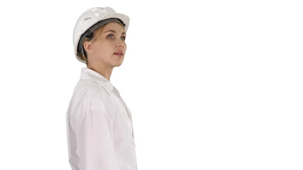 Young woman in hard hat walking and looking around on white back