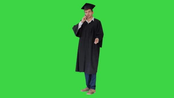 Мужчина выпускник в платье и миномётной доске разговаривает по телефону на зеленом экране, Chroma Key. — стоковое видео