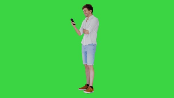 Красивый молодой человек с помощью своего смартфона и смеясь на зеленом экране, Chroma Key. — стоковое видео