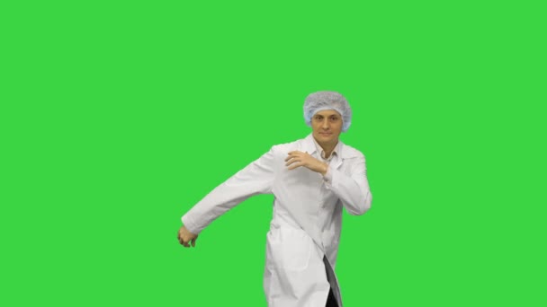 身穿白袍、头戴防护帽、跳现代舞的年轻男医生，在绿色荧幕上看着相机，铬钥匙. — 图库视频影像