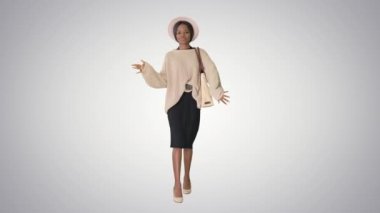 Örgü ve beyaz şapkalı şık Afro-Amerikan kadın arka planda yürürken dans ediyor..