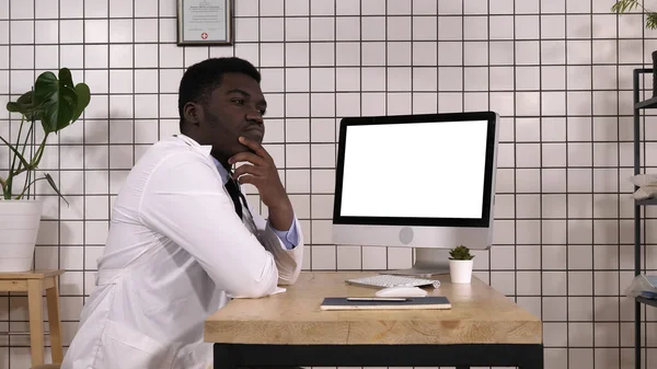 Άνδρας όμορφος Αφρικανός γιατρός σκέφτεται δίπλα στον υπολογιστή του. Γουίτ — Φωτογραφία Αρχείου