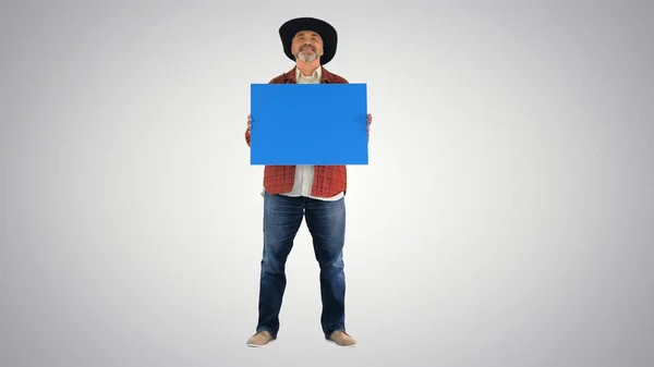 Старший фермер в шляпе держит пустой плакат на градиентном бэкгро — стоковое фото