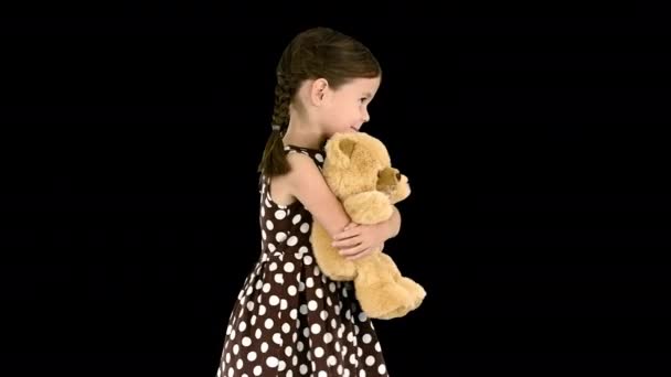 Klein meisje in polka dot jurk knuffelen grote teddybeer tijdens het lopen en kijken naar camera, Alpha Channel — Stockvideo