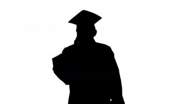 Siluet erkek mezuniyet elbisesi ve havan topu diplomasıyla yürürken telefonda konuşuyor..