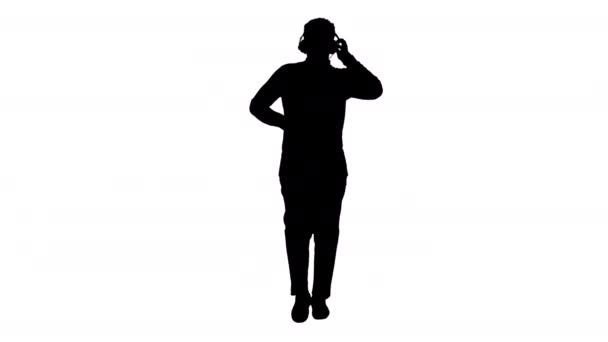 Silhouette Smiling hombre afroamericano sosteniendo auriculares con una mano y tocando música mientras camina frente a la cámara. — Vídeo de stock