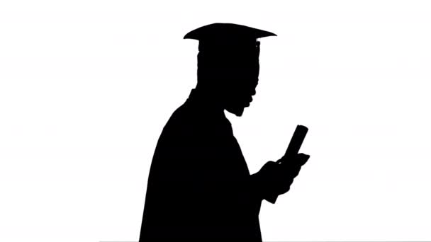 Silhouette Africain Américain mâle étudiant en robe de remise des diplômes textos au téléphone tout en marchant avec son diplôme. — Video