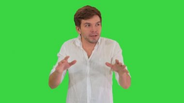 Heyecanlı genç adam, günlük giysiler içinde kameraya bakıyor bir hikaye anlatıyor ve yeşil ekranda işaret ediyor, Chroma Key..