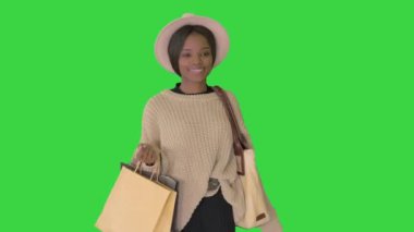 Şapkalı ve örgülü mutlu Afro-Amerikan kadın yeşil ekranda alışveriş çantasıyla yürüyor, Chroma Key..