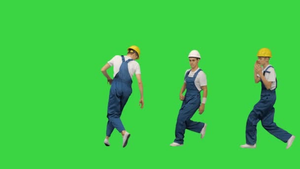 Három férfi építőmunkás kemény kalapban, remélve, hogy a kamera elé kerülnek, megtörik a táncot és elugranak egy zöld vásznon, Chroma Key. — Stock videók