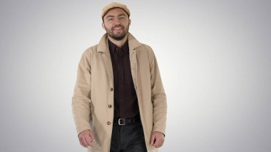 Palto giymiş gülümseyen adam kameraya bakıyor ve gradyan üzerinde yürüyor