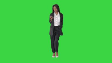 Gülümseyen Afrikalı Amerikalı kadın yeşil ekranda yürürken telefonla mesaj atıyor, Chroma Key.