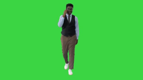 緑の画面、クロマキーのカメラを見て歩いている間に電話で話している若いアフリカ系アメリカ人のビジネスマンの笑顔. — ストック動画