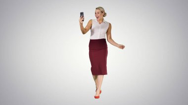 Yürüyen kadın gradyan üzerinde akıllı telefon kullanarak video görüşmesi yapıyor.