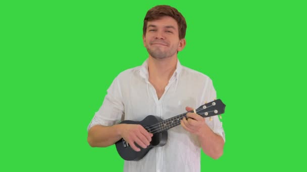 Jovem sorrindo jogando ukulele olhando para a câmera em uma tela verde, Chroma Key. — Vídeo de Stock