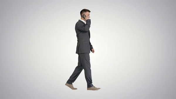 Бизнесмен ходит и разговаривает по мобильному телефону на градиенте назад — стоковое фото