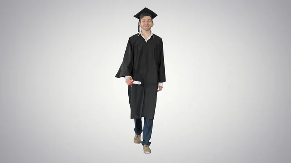 Улыбающийся студент в выпускном халате идет с дипломом — стоковое фото