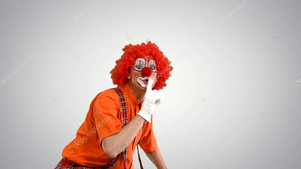 Clown prowling and making be quiet gesture to camera on gradient