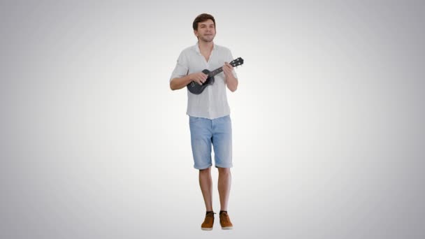 Glimlachende jongeman spelen ukelele en zingen kijken in de camera op gradiënt achtergrond. — Stockvideo