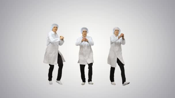 Three male doctors in white robes and protective caps doing synch dance routine looking at camera on gradient background. — Stock Video