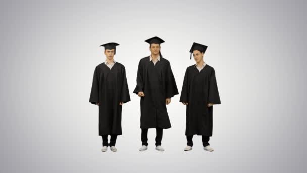 Три студента мужского пола в выпускных халатах и миномётных досках разогреваются в ожидании градиентного фона. — стоковое видео